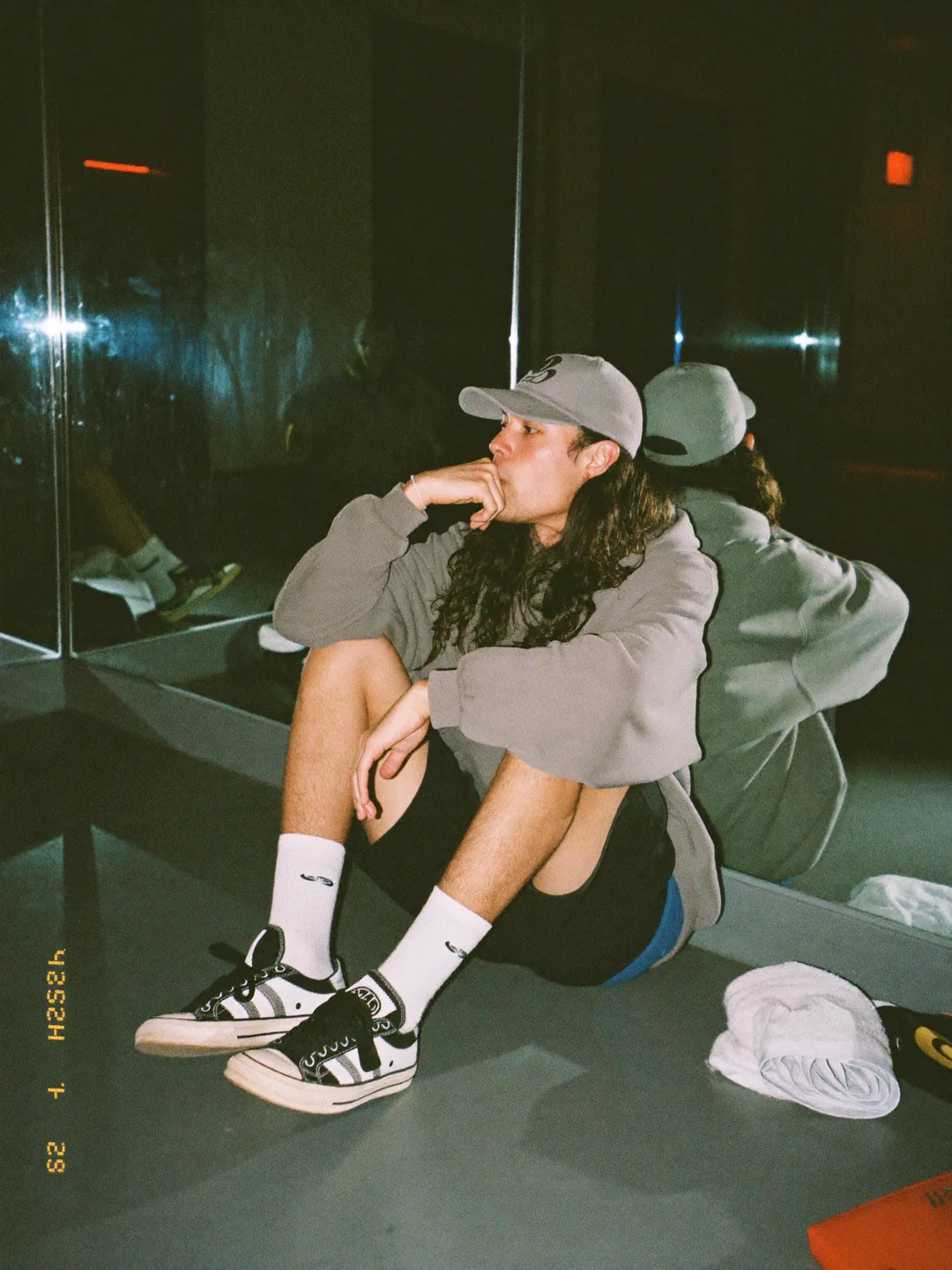 A street dancer sitting against a mirrored wall at night, catching his breath after a session